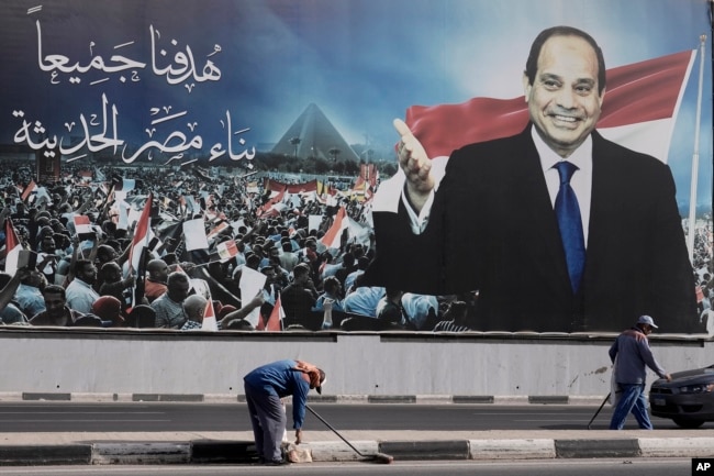 Des ouvriers nettoient la rue sous un panneau publicitaire soutenant le président égyptien Abdel Fattah el-Sissi pour les élections présidentielles, au Caire, Égypte, le 10 décembre 2023.