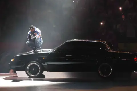 Getty Images Kendrick Lamar est illuminée par un projecteur tout en se produisant sur le capot d'une voiture Buick noire au Super Bowl